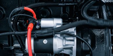 Close-up of a car starter motor with red and black cables attached.